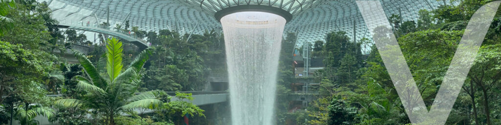 The Jewel in Singapore, a stunning indoor waterfall surrounded by a biophilic design environment, featuring vibrant plants and a glass dome ceiling. 