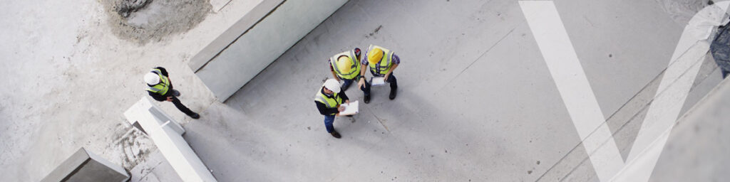 Vista aérea de un grupo de ingenieros y trabajadores inspeccionando una obra con estructuras de hormigón, promoviendo la construcción sostenible.